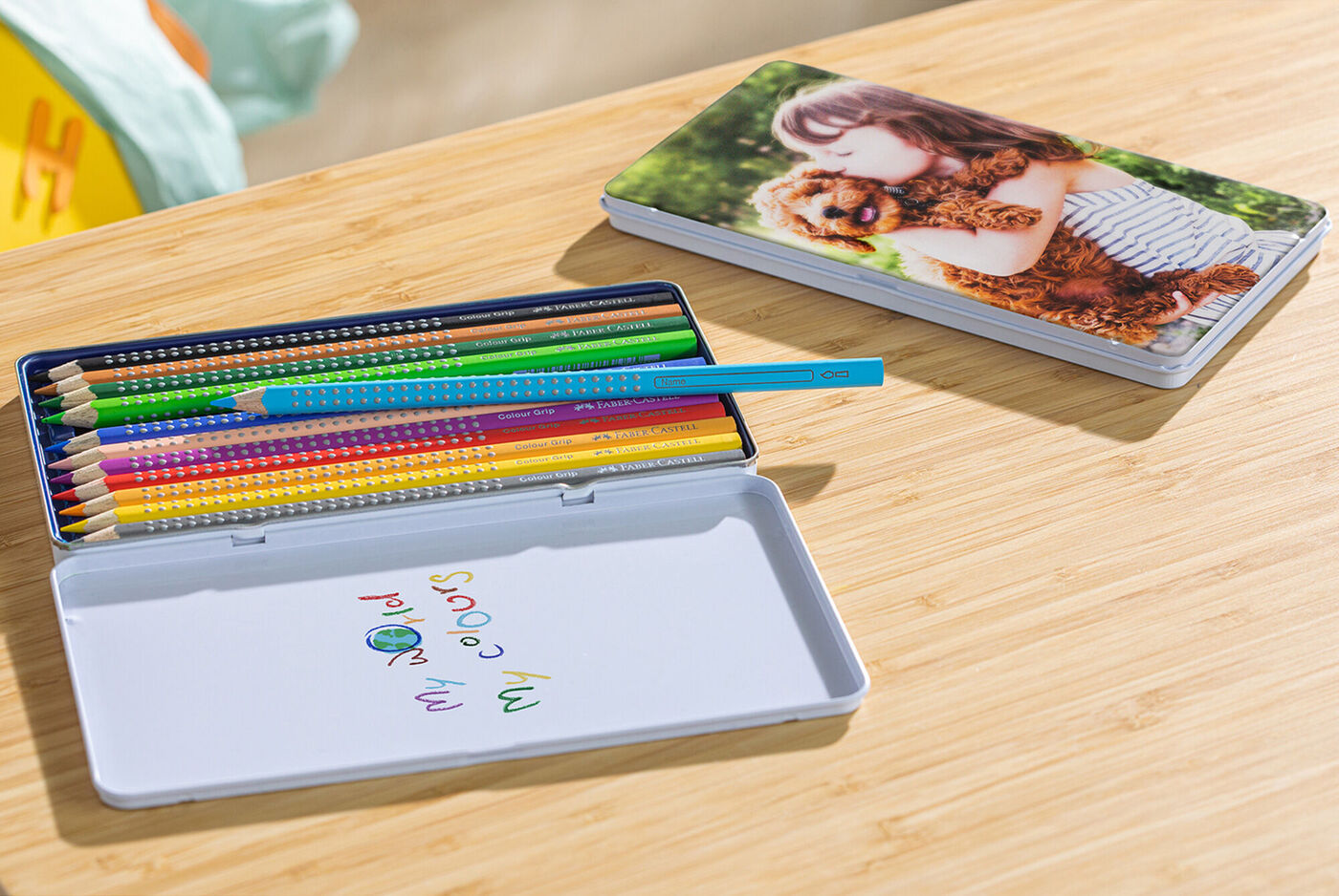 Boîte métallique ouverte avec crayons de couleur Faber Castell et à côté une boîte de crayons fermée avec une photo