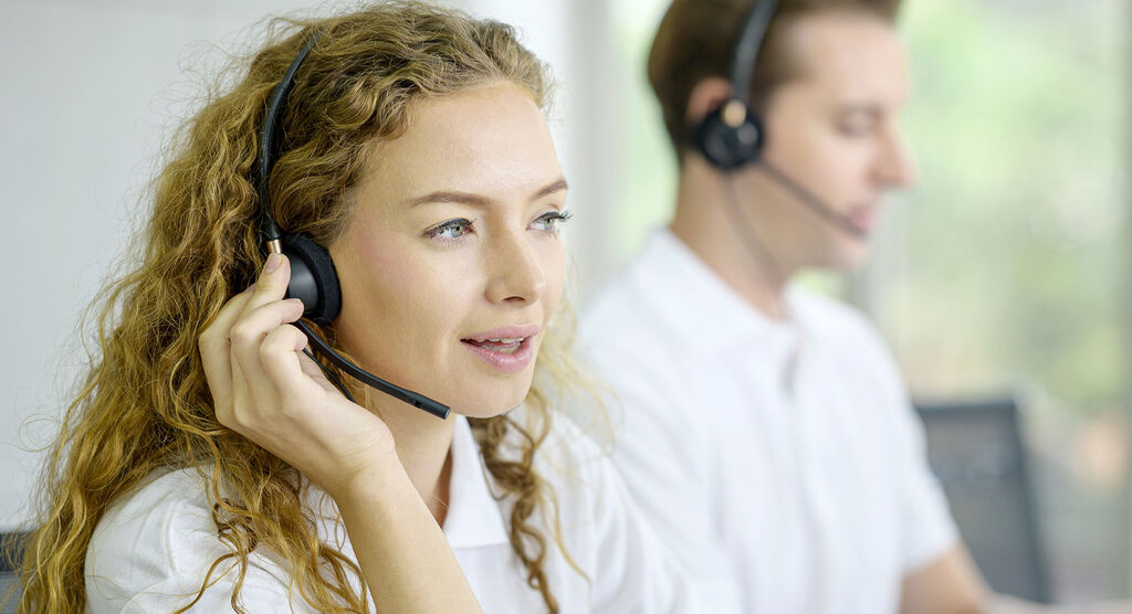 Deux personnes au service client avec des casques, souriants au téléphone, écoutent attentivement.