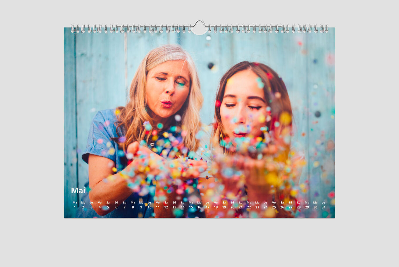 Deux personnes tenant des mains pleines de confettis colorés devant un fond bleu dans un calendrier.