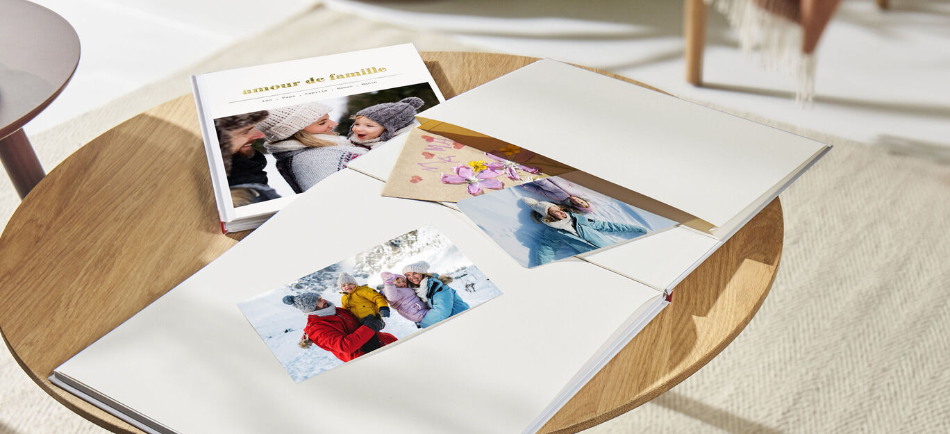 Un livre photo posé sur une table basse avec des images insérée dans la pochette souvenir du livre
