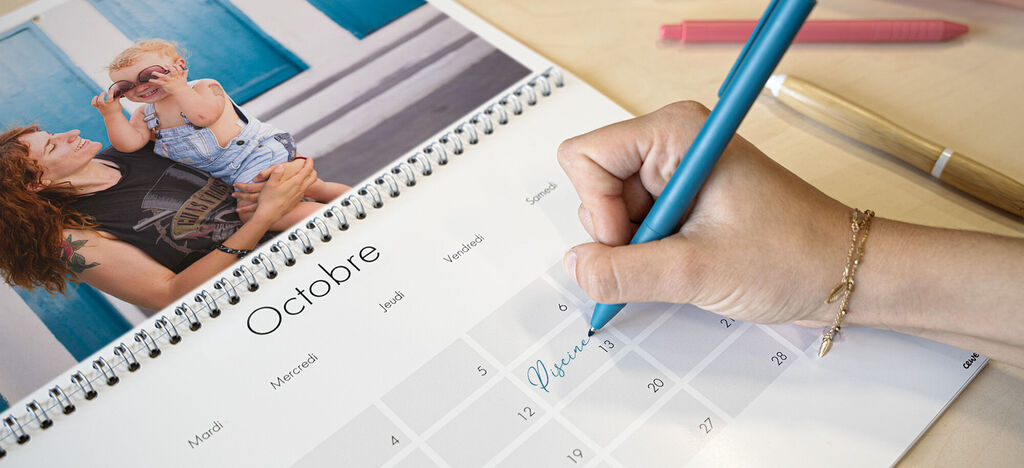 Une main en train de noter un RDV dans son calendrier personnalisé double-page avec une photo de famille