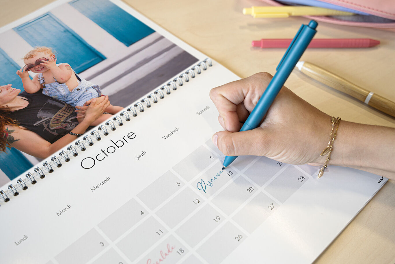 Une main en train de noter un RDV dans son calendrier personnalisé double-page avec une photo de famille