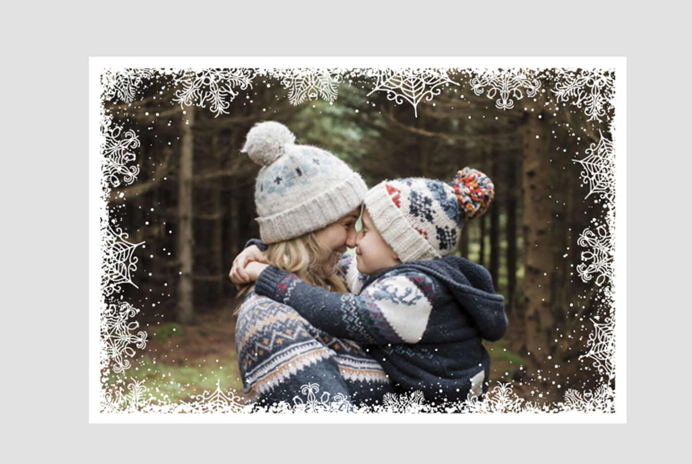 Une mère porte son enfant dans ses bras, tous deux en bonnets chauds, entourés d'une forêt hivernale.