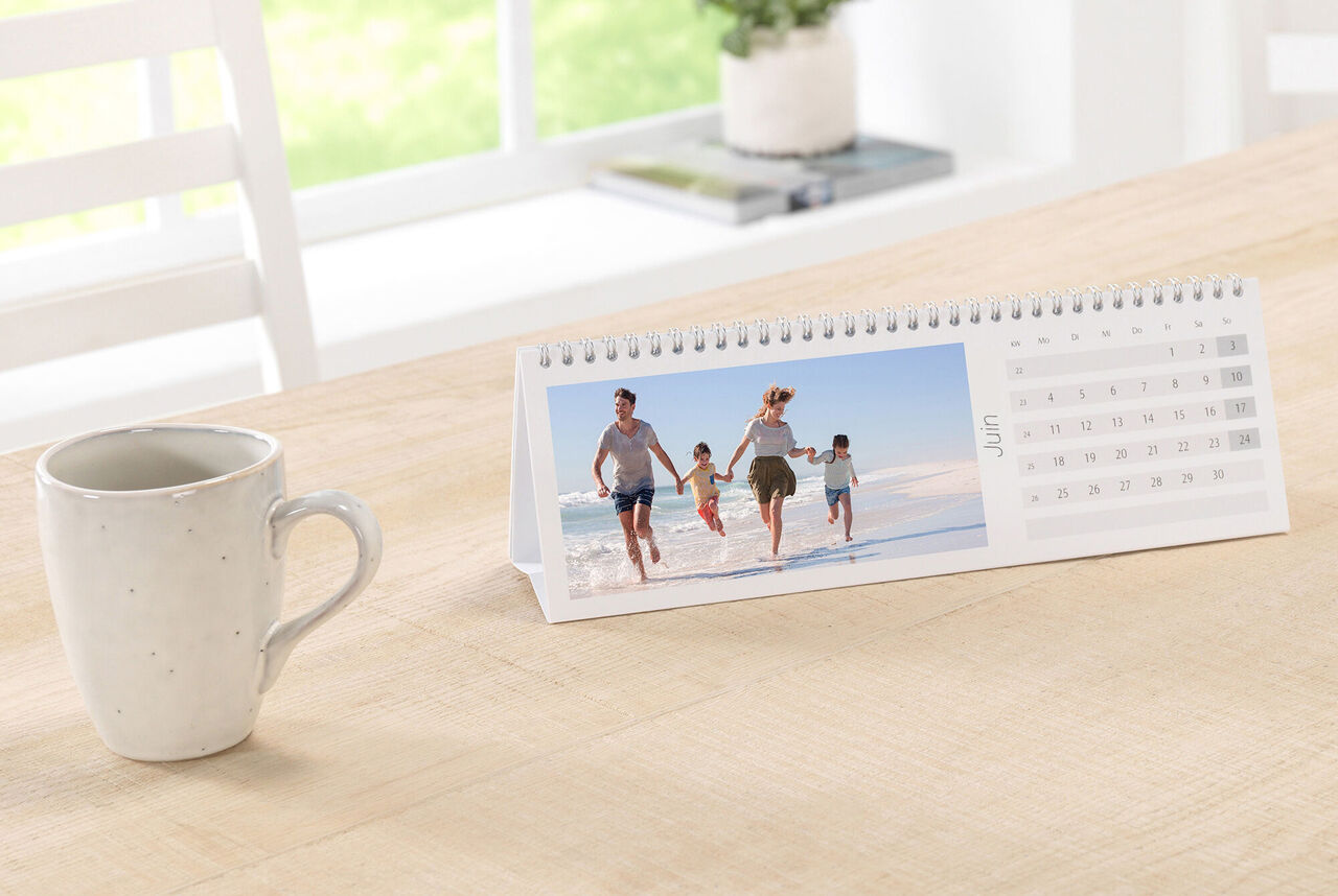 Une famille se réjouit de courir sur la plage en regardant le calendrier photo CEWE