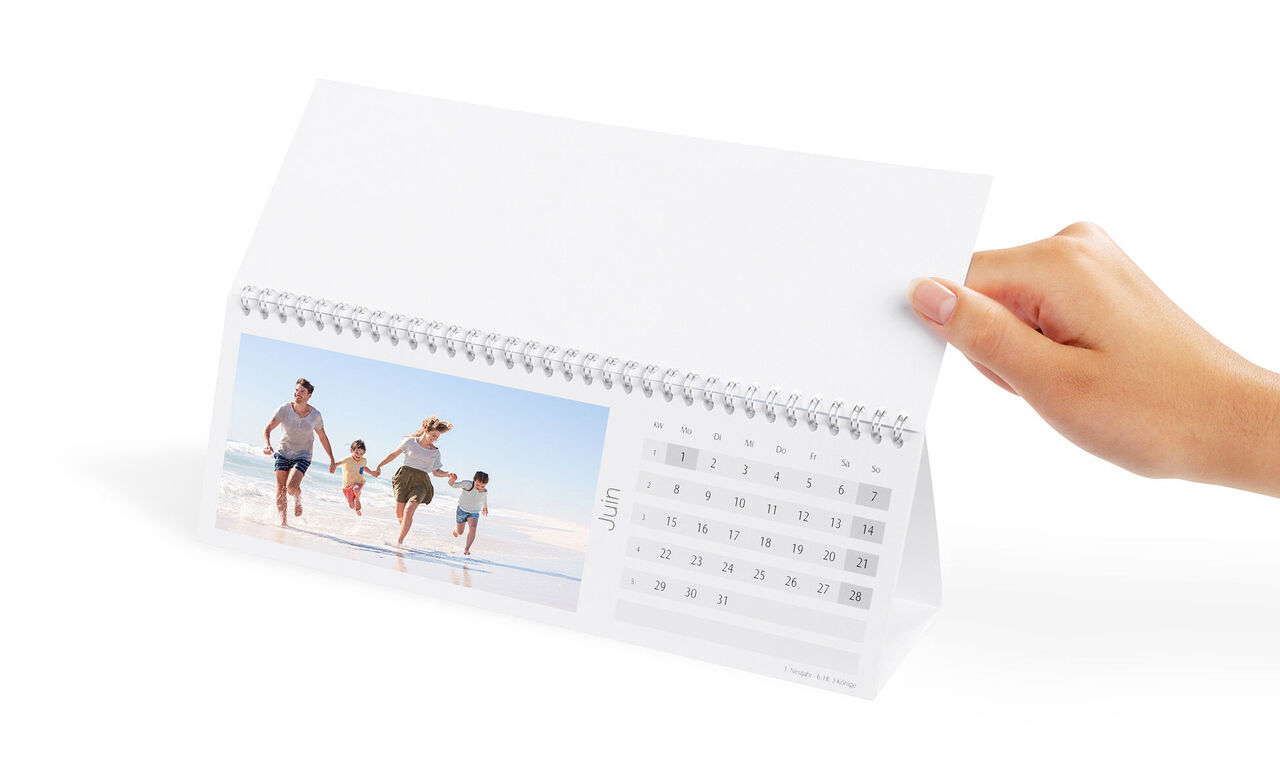 Une famille marche joyeusement sur la plage, tenant un calendrier photo dans sa main