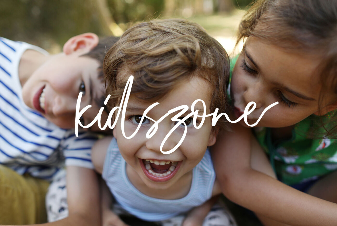 Trois enfants assis joyeusement à l'extérieur regardent quelque chose au premier plan, l'image dégage joie et insouciance.