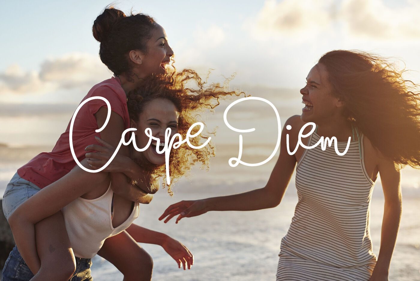 Deux femmes profitent d'une journée ensoleillée à la plage, tandis qu'une troisième est assise sur le dos de l'autre. Elles rient et s'amusent.