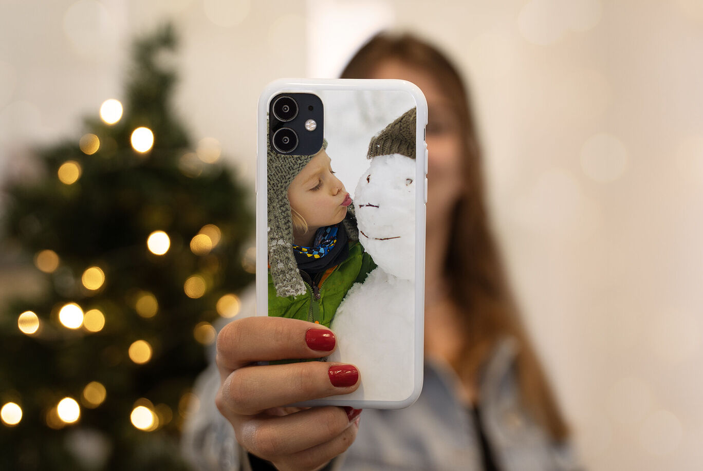Une personne tient un téléphone avec une photo d'un enfant dormant en hiver, entouré de branches de sapin et de lumières.
