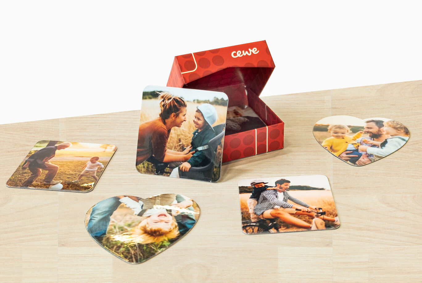 Des cartes photo en forme de cœur sont posées à côté d'une boîte cadeau CEWE remplie de souvenirs.