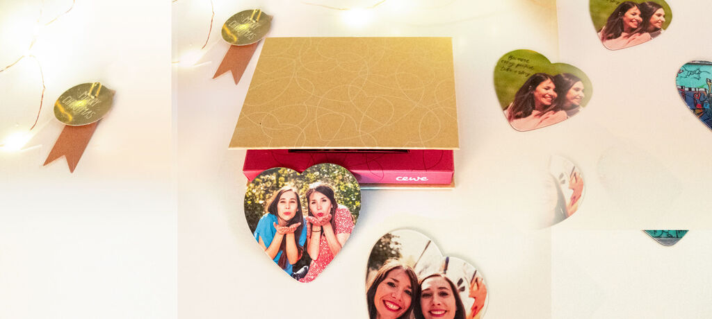 Un magnifique CEWE Fotobuch avec des souvenirs aimants, entouré de collages en forme de cœur.