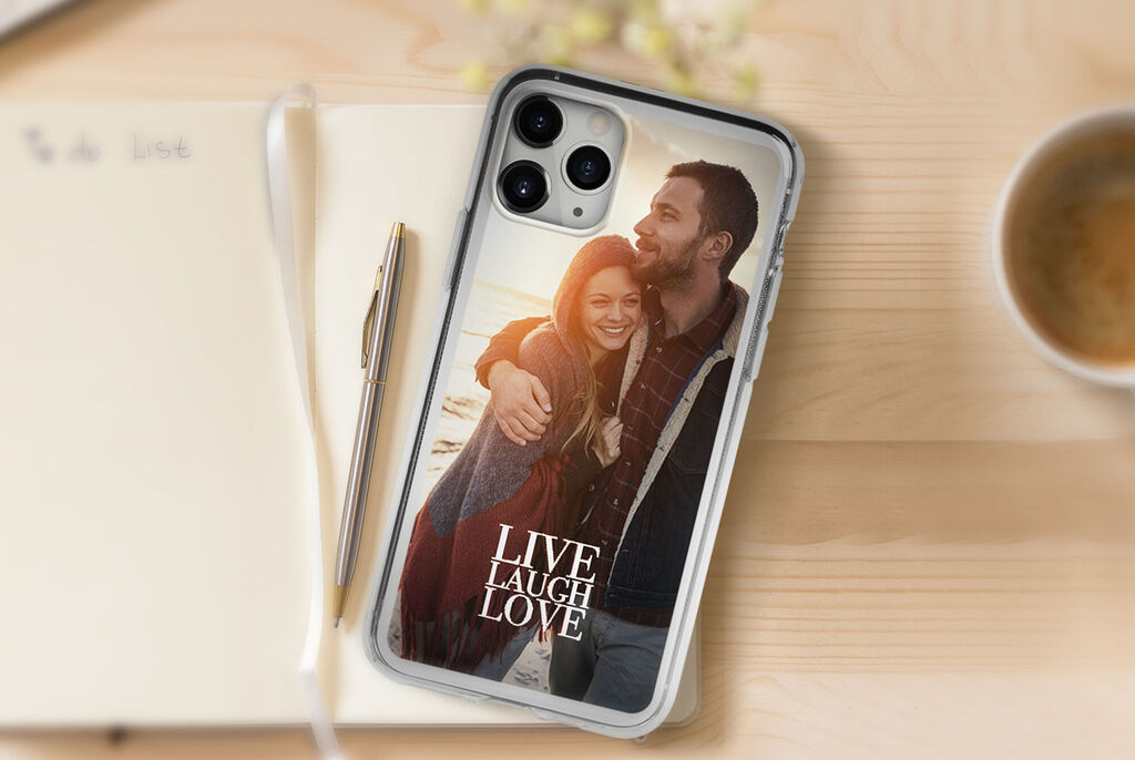 Un téléphone avec une coque personnalisée, portant le dicton 'Live Laugh Love', sur une table avec un carnet et une tasse