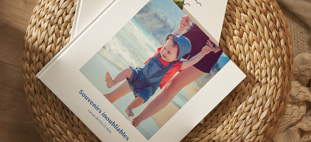 Un petit enfant est joyeusement tenu par un adulte pendant qu'il joue sur la plage. L'océan est visible en arrière-plan.