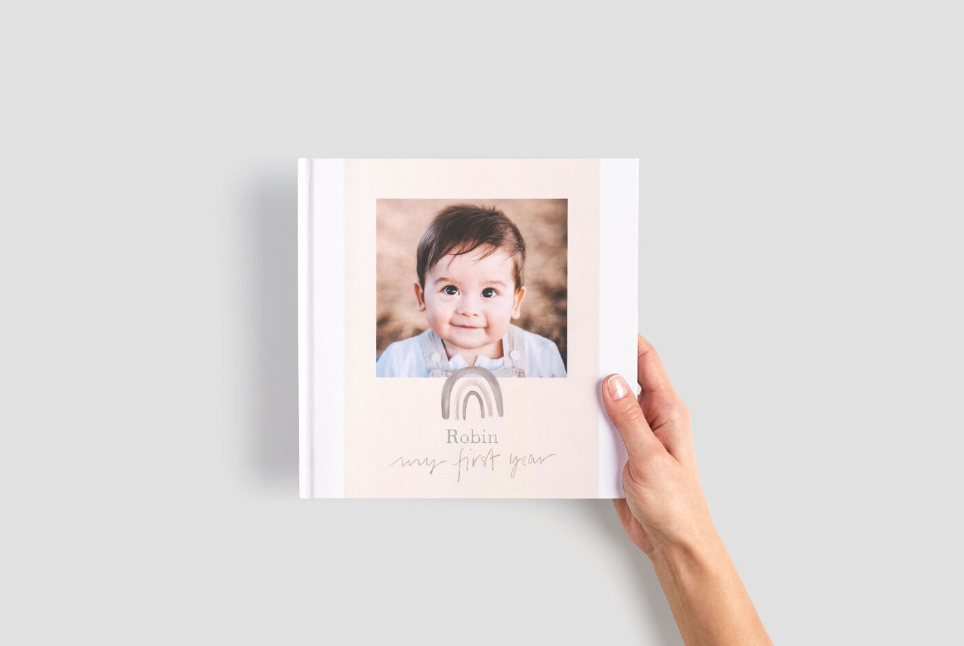 Album photo carré tenu par une main, avec les photos d'un petit garçon