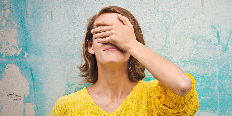 Jeune femme avec la main sur le visage dans un pull jaune devant un mur bleu.