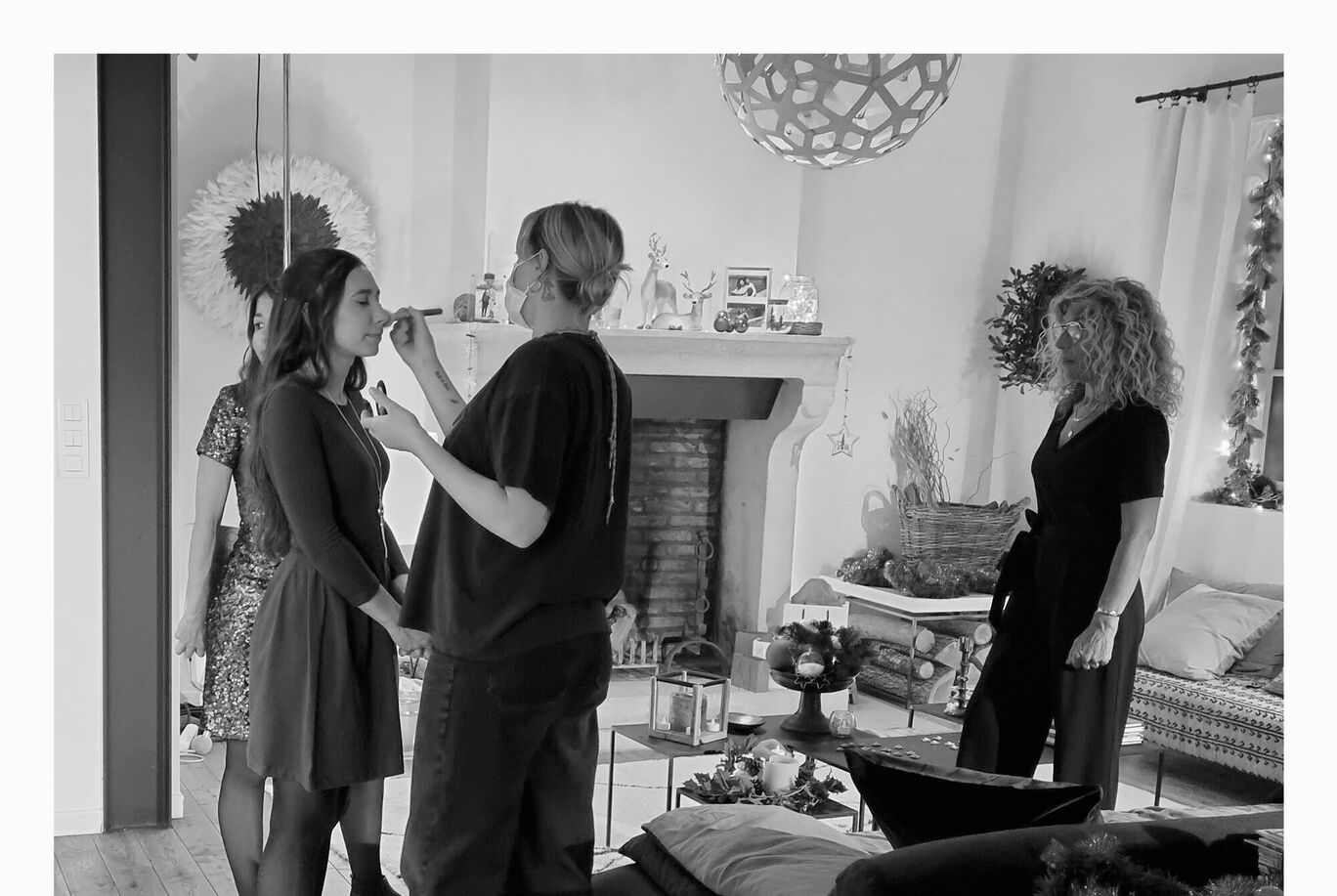 Deux femmes se tiennent dans une pièce lumineuse. L'une se fait maquiller, l'autre l'observe. L'ambiance est amicale et détendue.