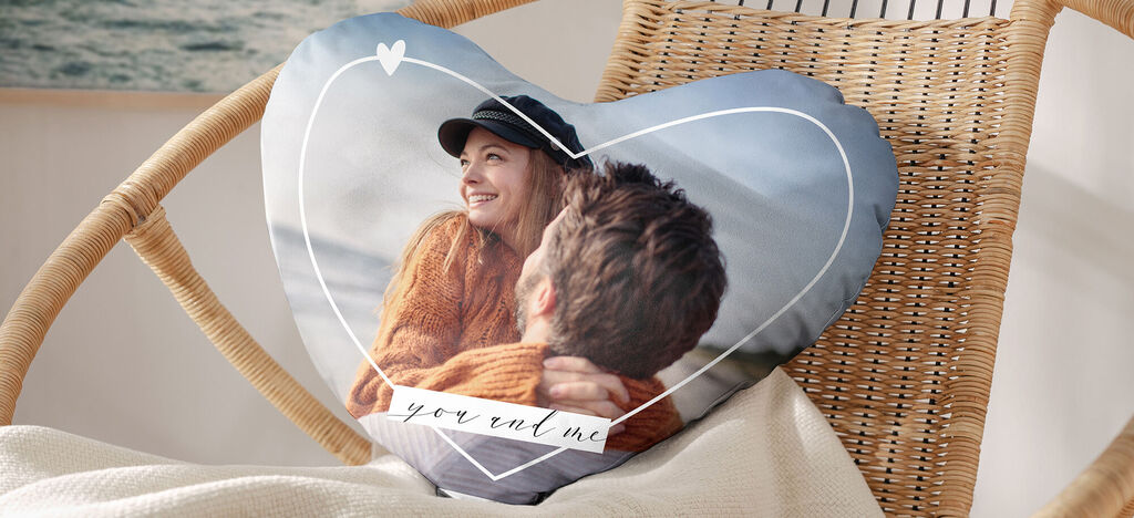 Un coussin en forme de cœur avec une photo d'un couple en arrière-plan, assis dans un cadre détendu.
