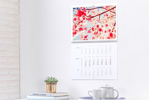 Un magnifique calendrier photo avec des fleurs de cerisier en arrière-plan. Il est accroché à un mur blanc.