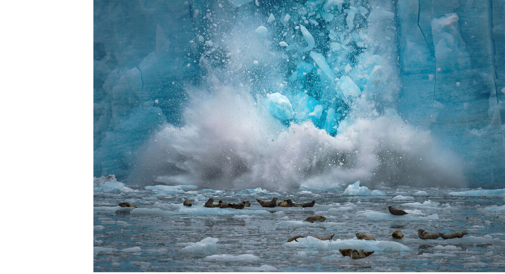 Un glacier s'effondre, créant une grande fontaine d'eau sous des nuances de bleu.