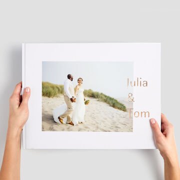 Grand album photo paysage, tenu entre les mains, avec la photo d'un couple sur la plage en couverture