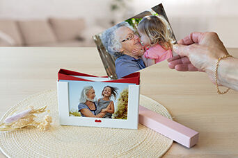 Une main tient une photo au-dessus d'un album photo CEWE d'une femme et d'un enfant.