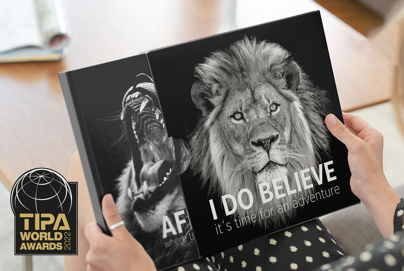 Une personne présente un album photo avec un lion et un gorille. Couverture avec I DO BELIEVE et distinction TIPA.