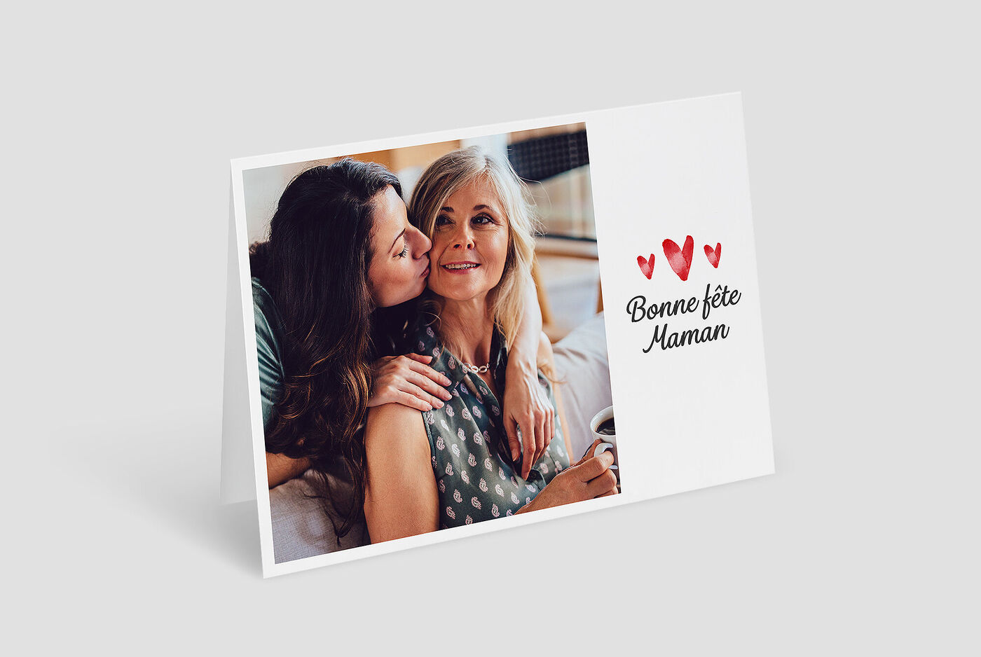 Trois dames s'enlacent affectueusement en célébrant. Une personne tient un café.