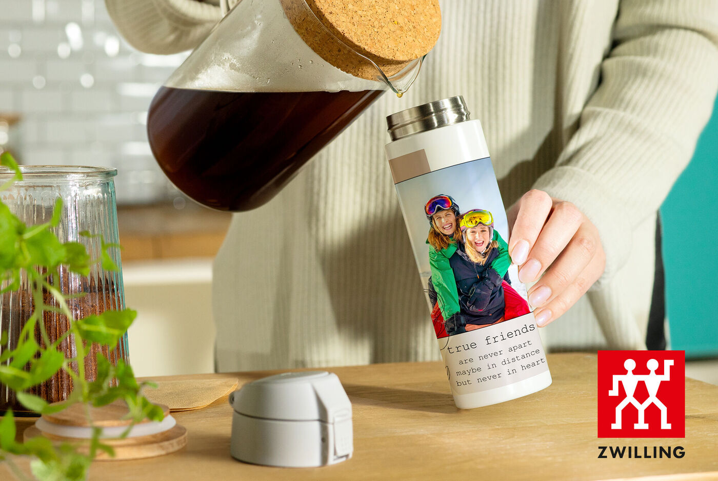 Une personne verse du café d'une théière dans une bouteille thermos personnalisée marquée "Vrais amis".