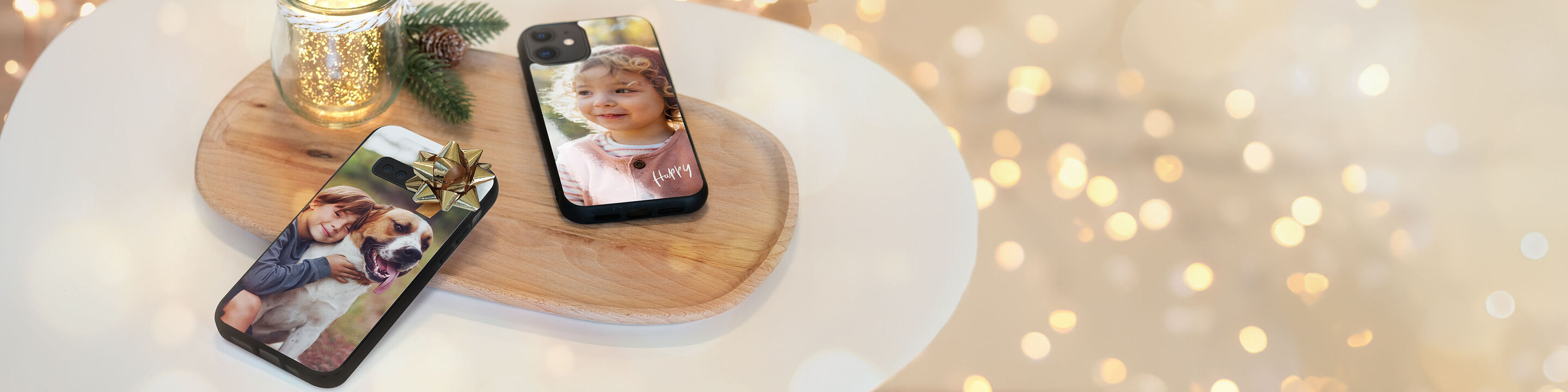 Deux smartphones sur un plateau en bois avec des couvertures photo, l'un avec un chien, l'autre avec un enfant, entourés de lumières romantiques.