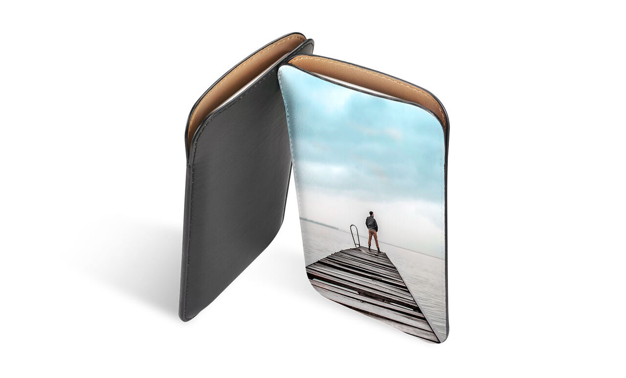 Femme sur une jetée au bord de l'eau, tenant une housse CEWE FOTOBUCH, nuages dans le ciel.