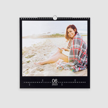 Une femme est sur la plage, emmitouflée dans une couverture, avec un livre. Juin 2023 est visible au calendrier.