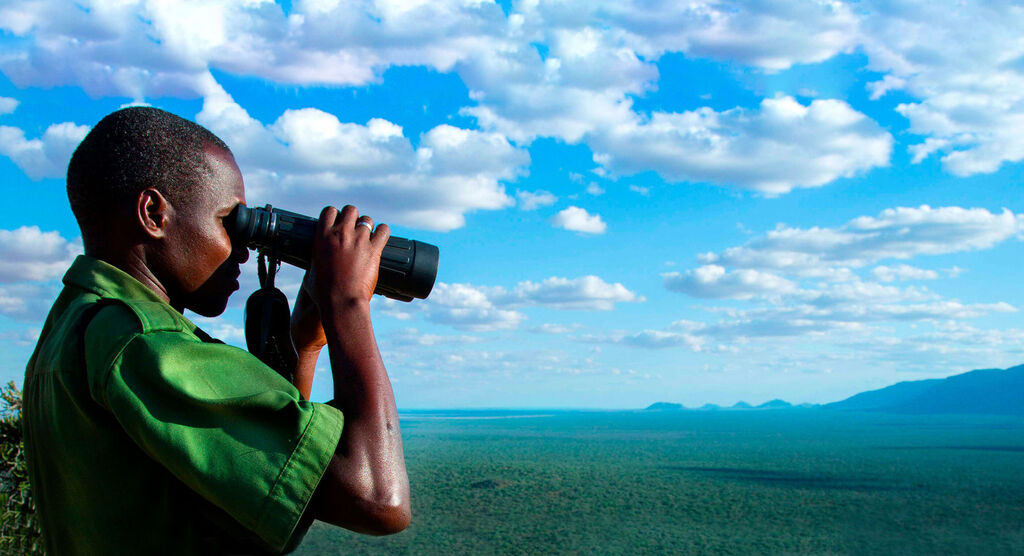Une personne observe le paysage avec des jumelles sous un ciel large et nuageux.