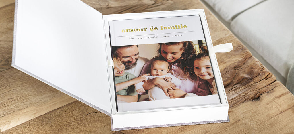 Une CEWE Foto-Box soigneusement conçue avec des photos de famille, sur une table en bois.