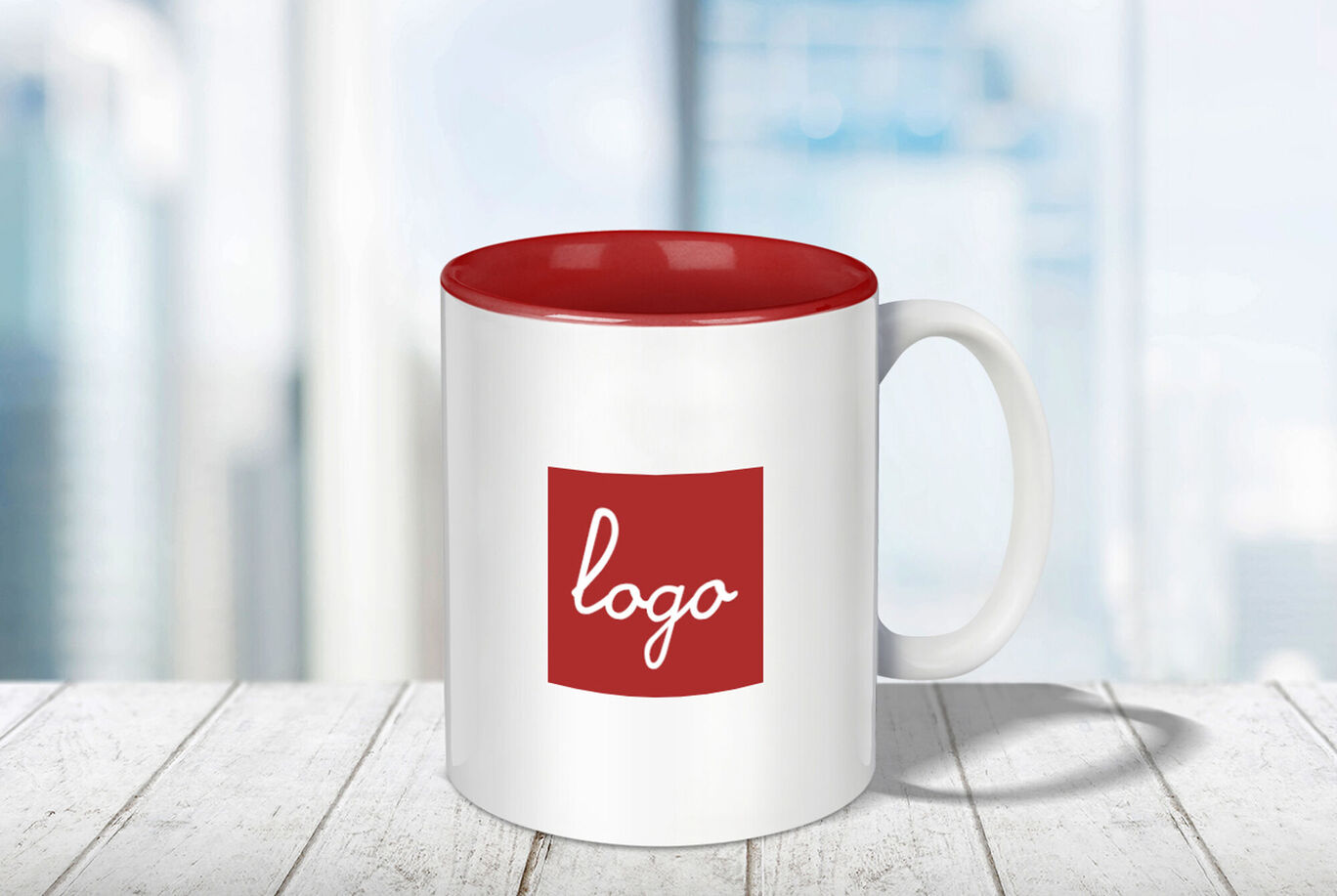 Une tasse blanche avec une anse rouge et un bord rouge, avec un logo rouge. L'arrière-plan est flou et lumineux, créant une sensation chaleureuse.