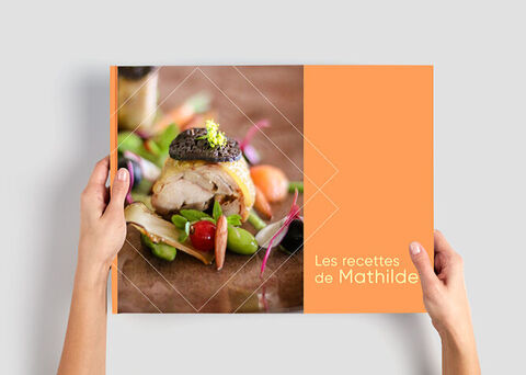 Une personne tient un livre de recettes soigneusement conçu intitulé 'Les recettes de Mathilde'.