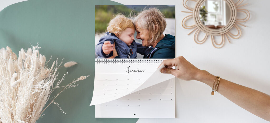 Main tenant un calendrier montrant une photo, feuilletant la page, plantes et miroir en arrière-plan