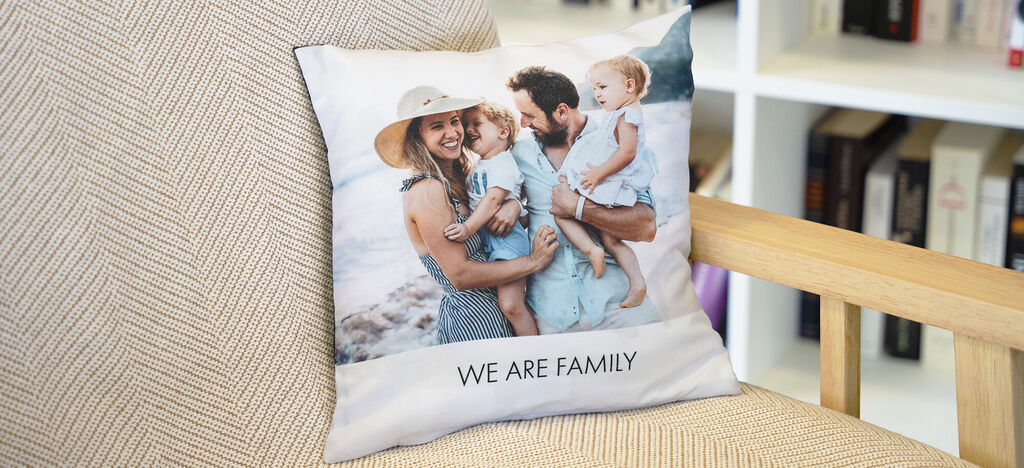 Un coussin artistique avec l'inscription 'NOUS SOMMES UNE FAMILLE' et une famille joyeuse à la plage.