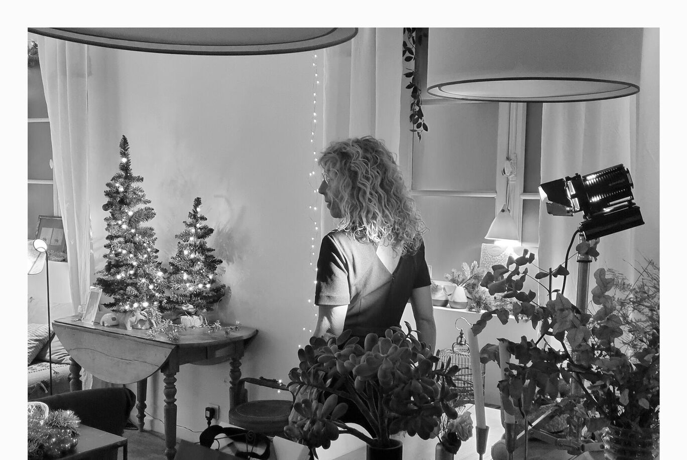 Une femme aux cheveux bouclés admire deux sapins décorés dans une atmosphère agréable.