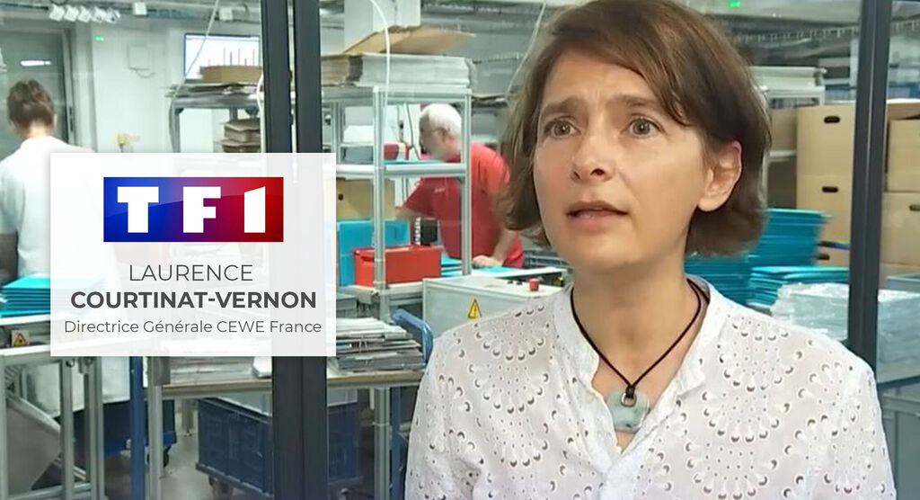 Une personne aux cheveux bruns se tient dans un bureau moderne avec plusieurs postes de travail.