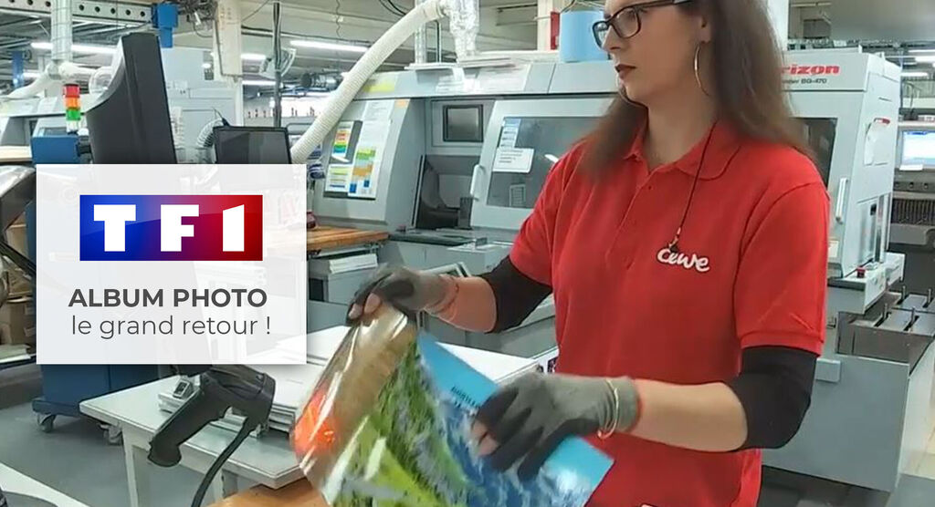 Une employée tient un album photo CEWE, entourée de machines à imprimer. Elle porte des gants et un T-shirt CEWE rouge.