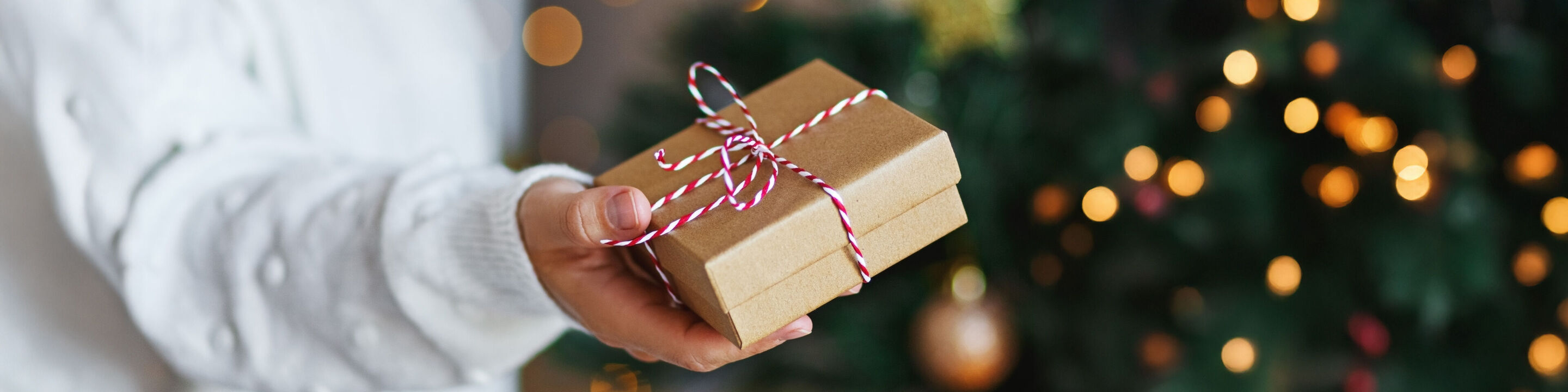 Une personne tient un cadeau soigneusement emballé avec un ruban coloré, le fond est festivement décoré