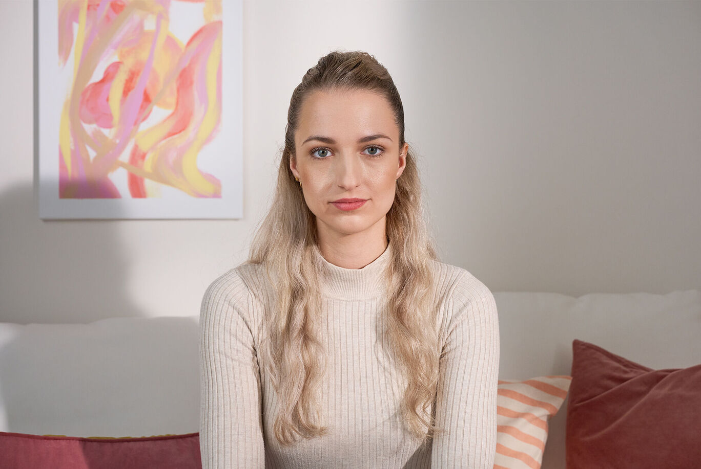 Une personne aux cheveux longs et blonds est assise sur un canapé, entourée de coussins colorés.