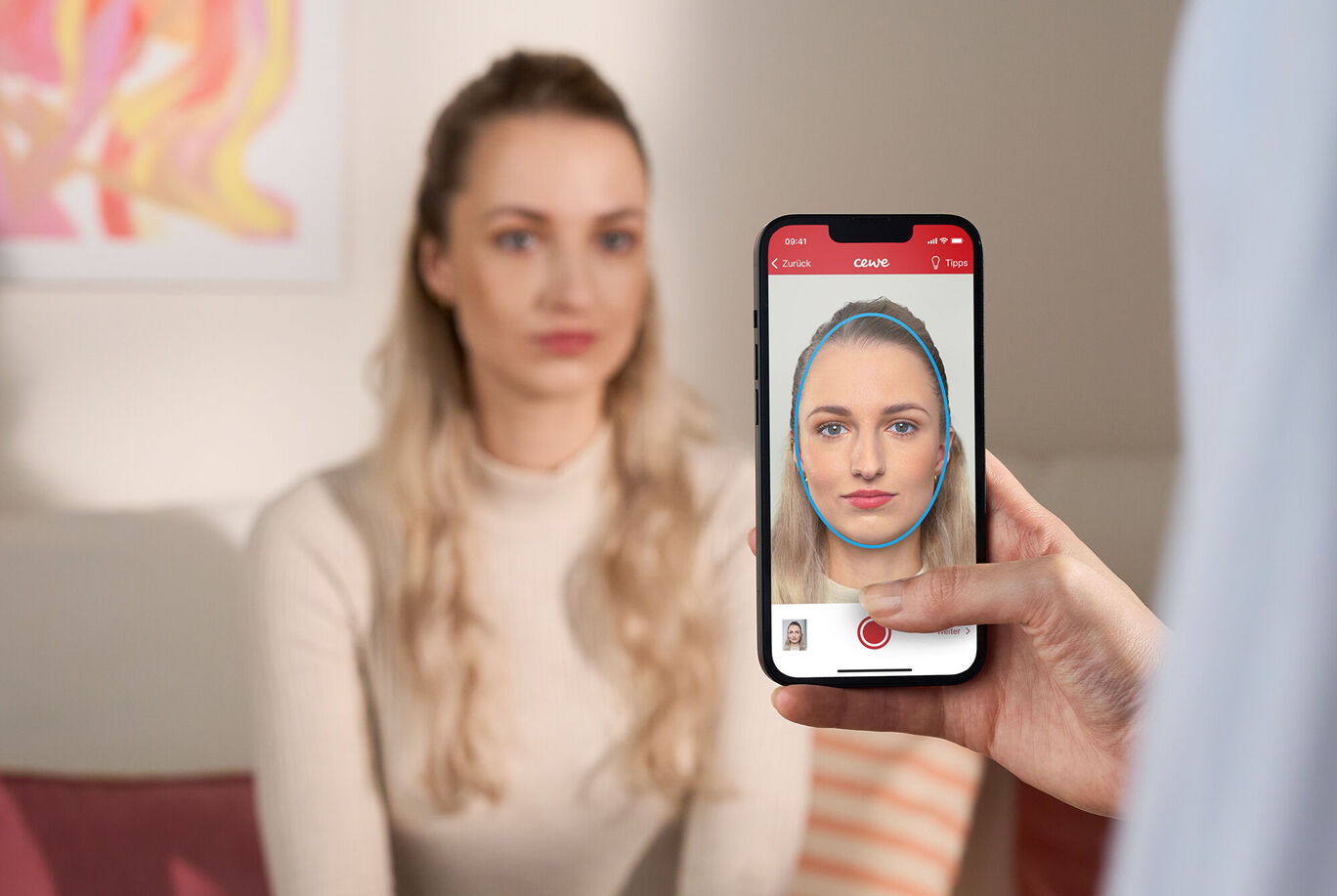 Une personne sourit et est photographiée avec un smartphone, assise sur un canapé.