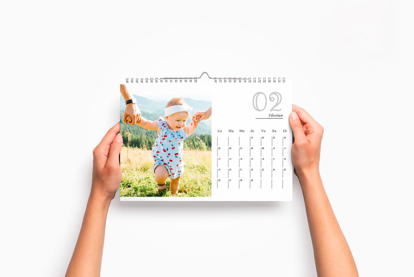 Un calendrier personnalisé horizontal entre les mains d'une personne, avec la photo d'un bébé marchant dans l'herbe