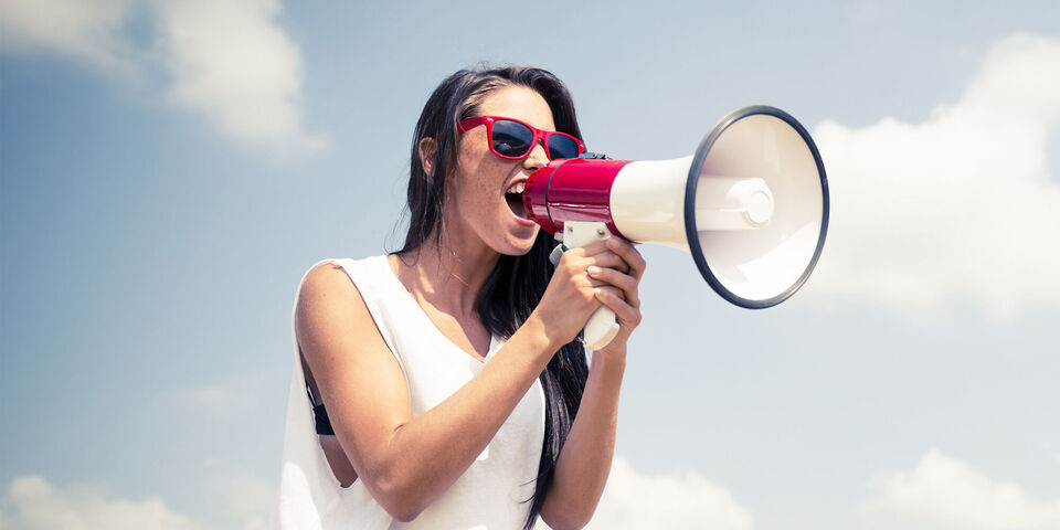 Femme tient un mégaphone et parle avec enthousiasme.