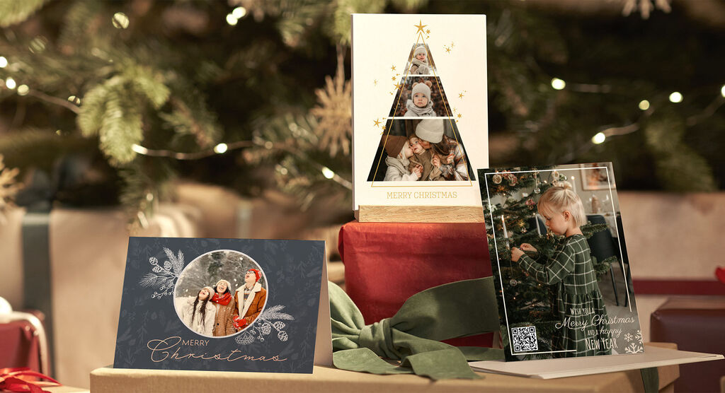 Trois cartes de vœux festives soigneusement présentées sur des cadeaux sous un sapin de Noël.