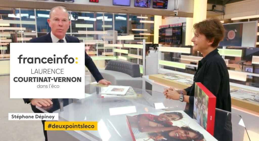Une femme montre un livre photo à une table, tandis qu'un homme l'écoute attentivement.