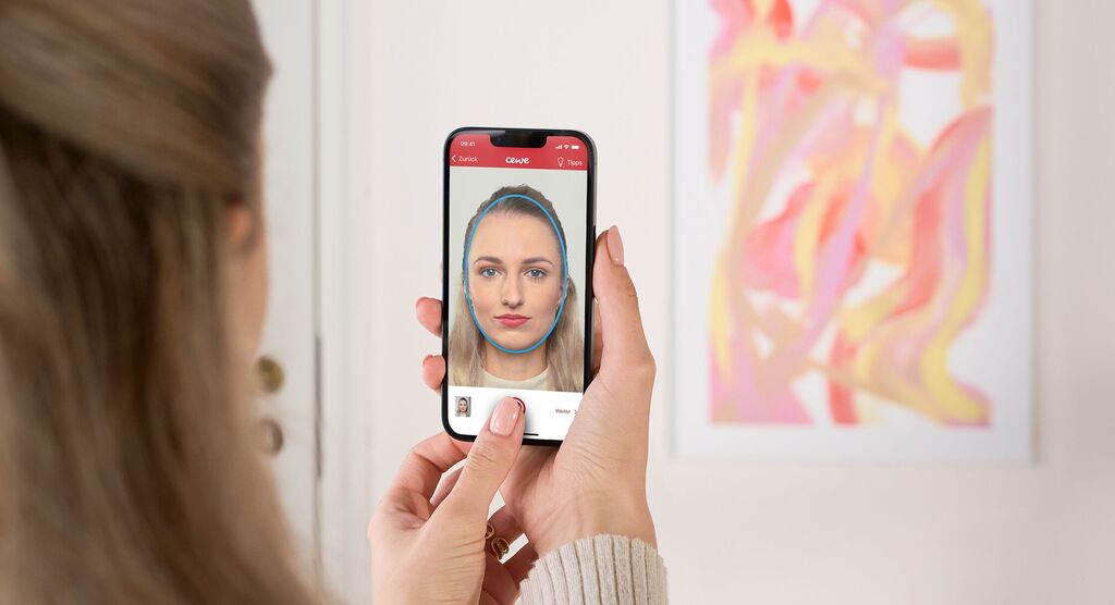 Une personne tient un smartphone et regarde un selfie. Un mur coloré est en arrière-plan.