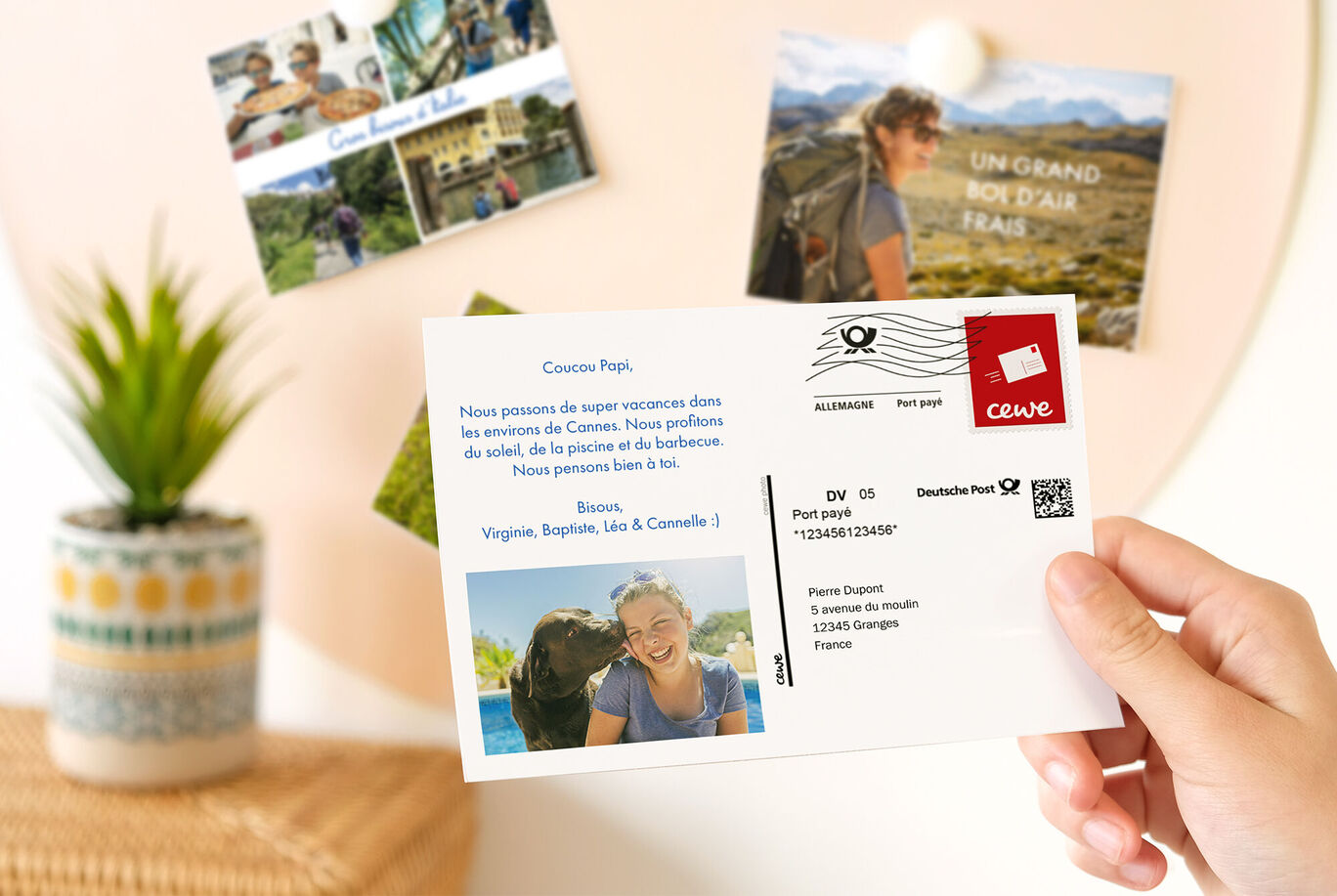 Une main tient une carte de vœux CEWE avec un message personnel et une photo de vacances.