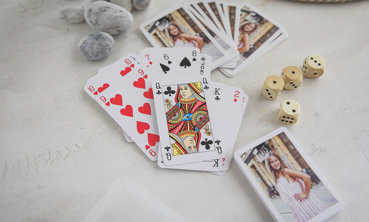 Jeu de cartes personnalisé avec photos d'une jeune fille, dés en bois et cartes étalées sur table claire.