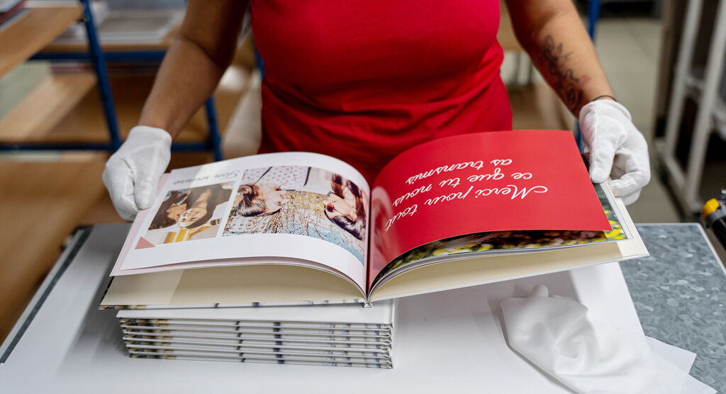 Une personne tient un livre photo ouvert avec des photos colorées et une couverture rouge, texte inspirant